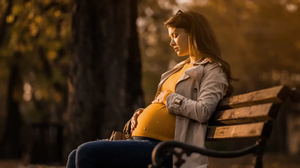 A pregnant woman sitting on a park bench with a sad face